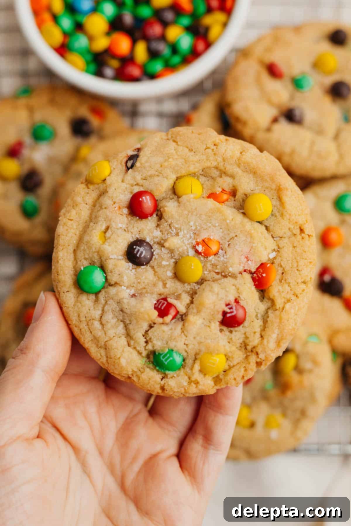Pillowy M&M Cookie Bites 2 A hand holding a perfectly round, thick mini M&M cookie, showcasing its vibrant colors and soft texture.