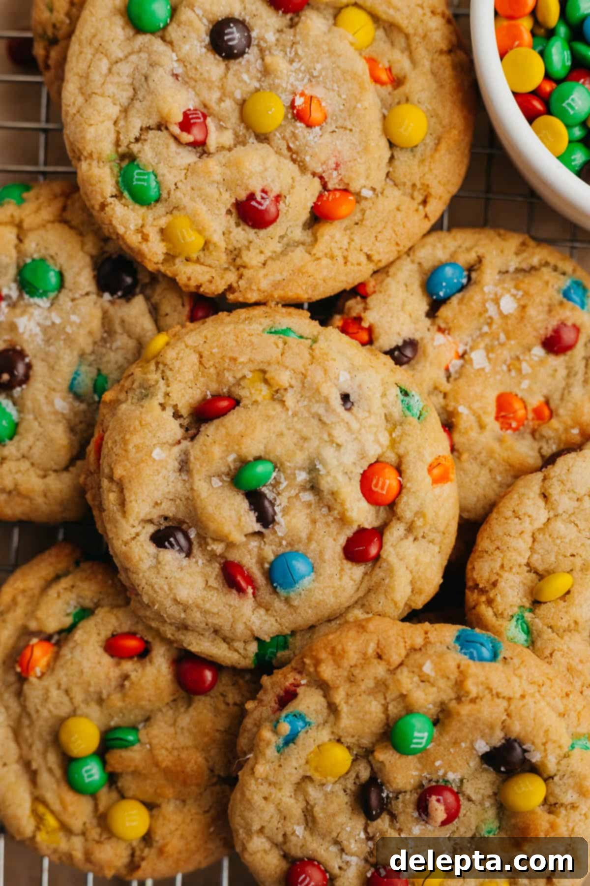 Pillowy M&M Cookie Bites 7 A vibrant array of rainbow mini M&M cookies neatly arranged on parchment paper, with a small bowl of mini M&M's beside them.