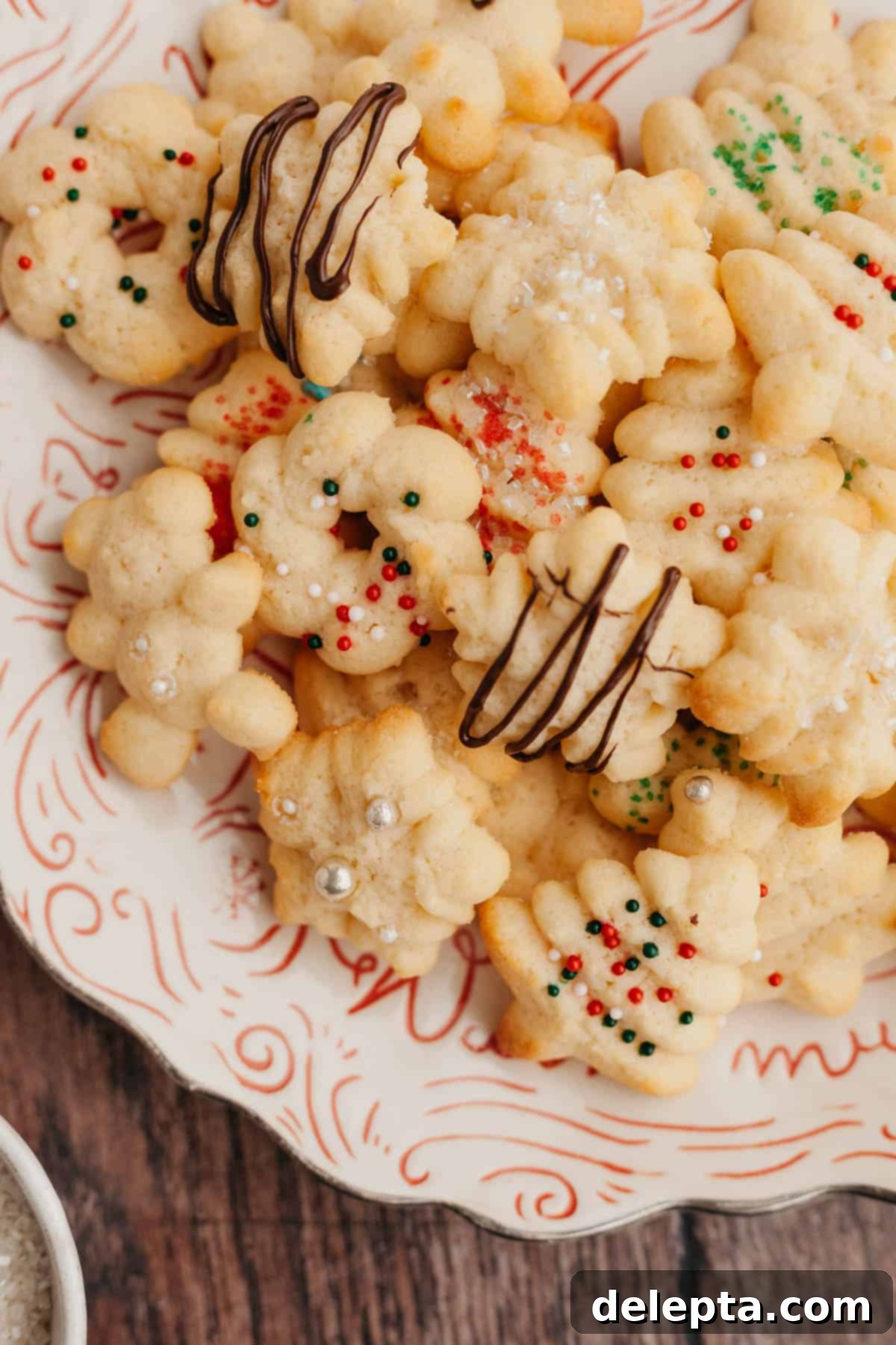 Velvet Cream Cheese Spritz Delights 7 Christmas spritz cookies with festive sprinkles arranged on a charming red and white plate.