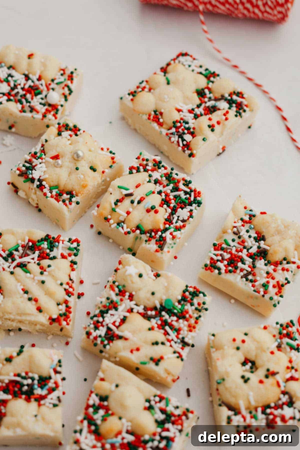 Festive Christmas Cookie Fudge 2 Square pieces of fudge covered in red and green sprinkles and Christmas cookies on parchment paper. A perfect, vibrant display of holiday cheer in every bite.