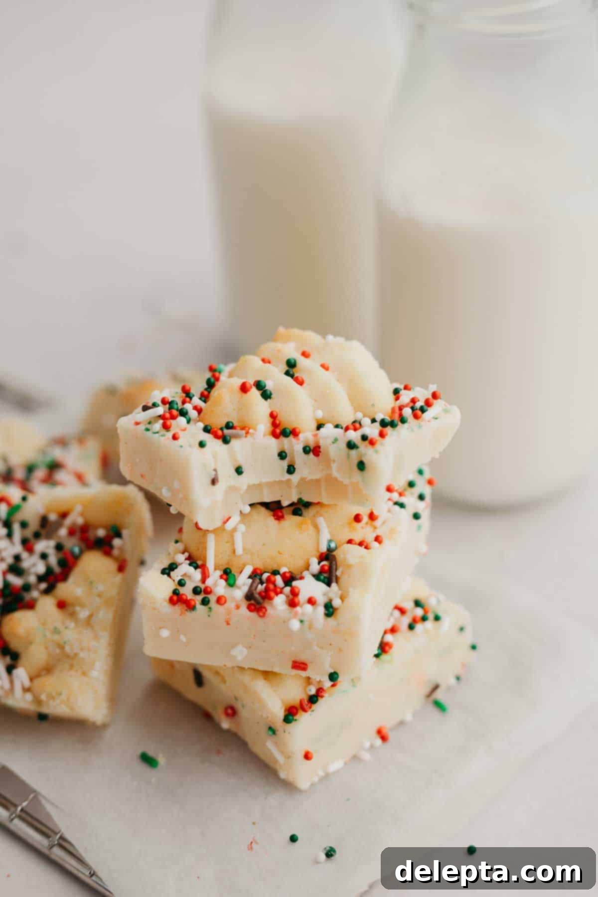 Festive Christmas Cookie Fudge 7 A stack of 3 pieces of Christmas cookie fudge, the piece on top has a bite taken out of it, revealing the creamy texture.