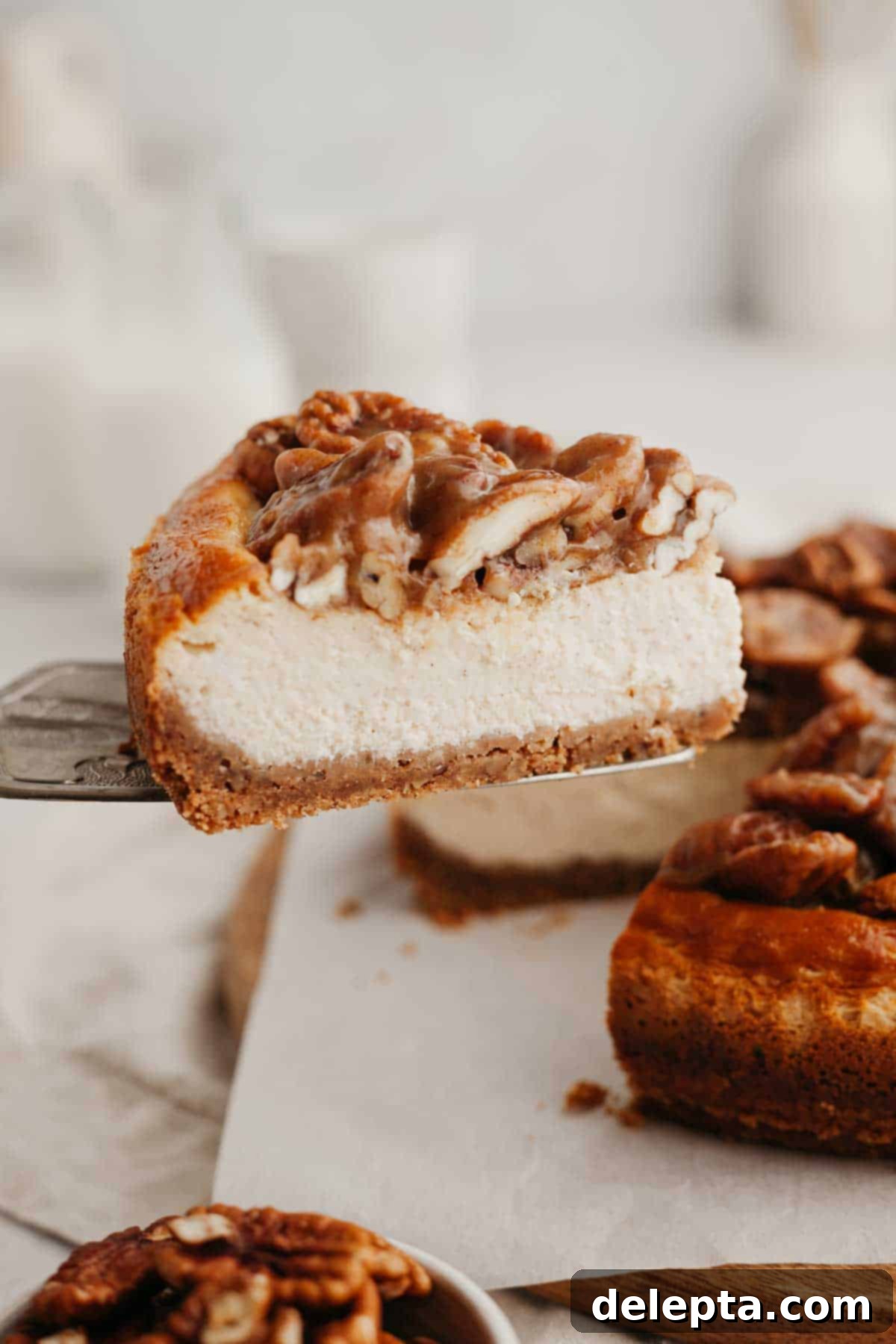 Decadent Pecan Pie Cheesecake 9 A stunning close-up of a slice of pecan pie cheesecake being lifted out of the whole cake, highlighting its rich, textured topping and smooth filling.