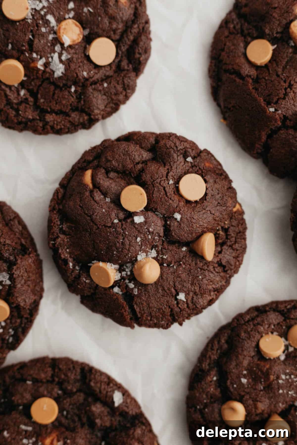 Decadent Caramel Chocolate Cookies 2 A close-up of a perfectly baked, warm chocolate caramel cookie on parchment paper, revealing its fudgy texture and melted caramel chips.