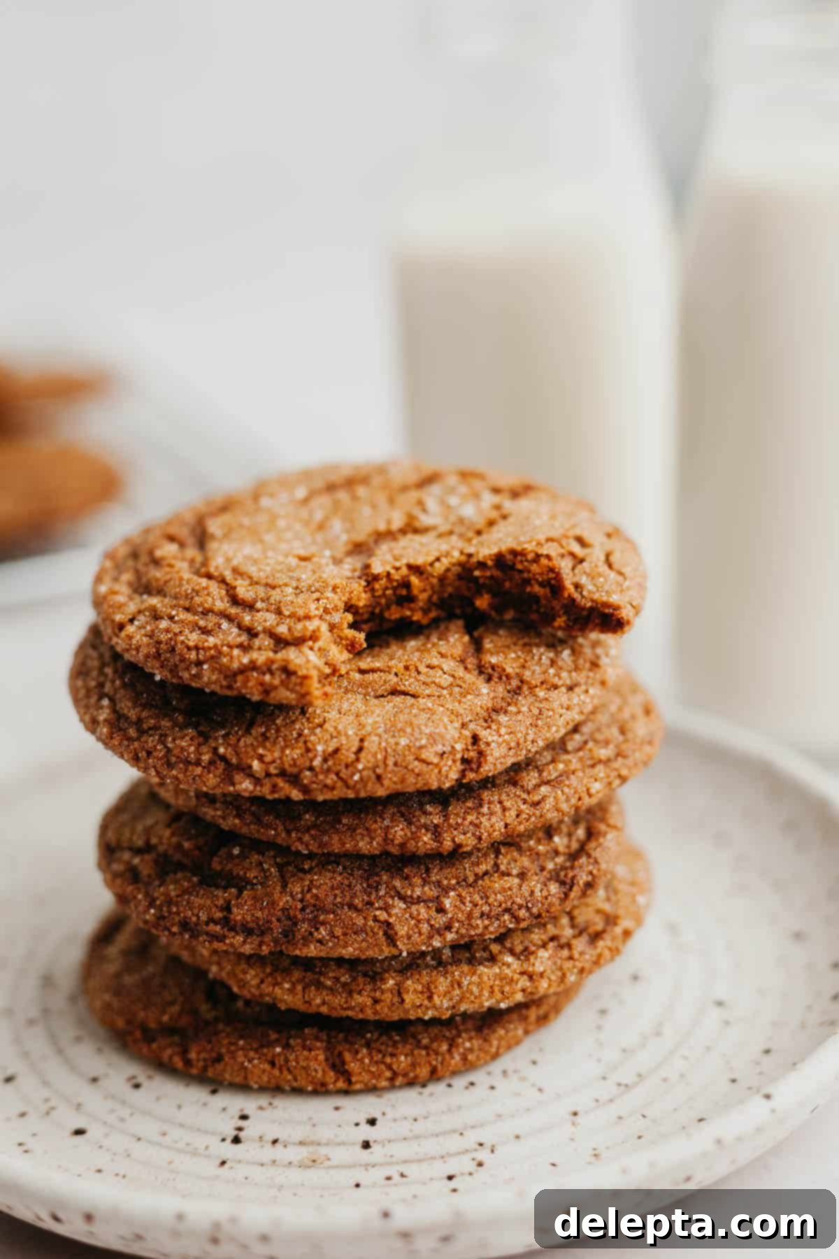 Chewy Spiced Molasses Crinkles 8 A charming stack of molasses crinkle cookies, with the top cookie having a bite taken out, revealing its soft and chewy interior.