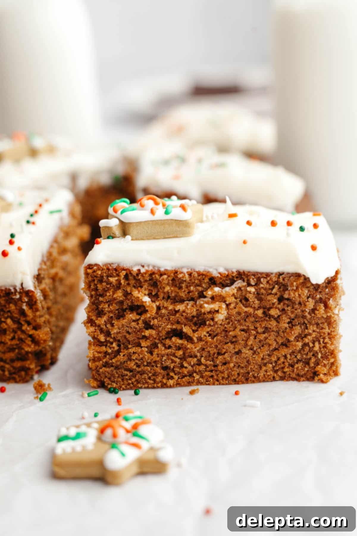 Cozy Gingerbread Cake with Cream Cheese Frosting 10 A slice of gingerbread cake with cream cheese frosting on parchment paper.
