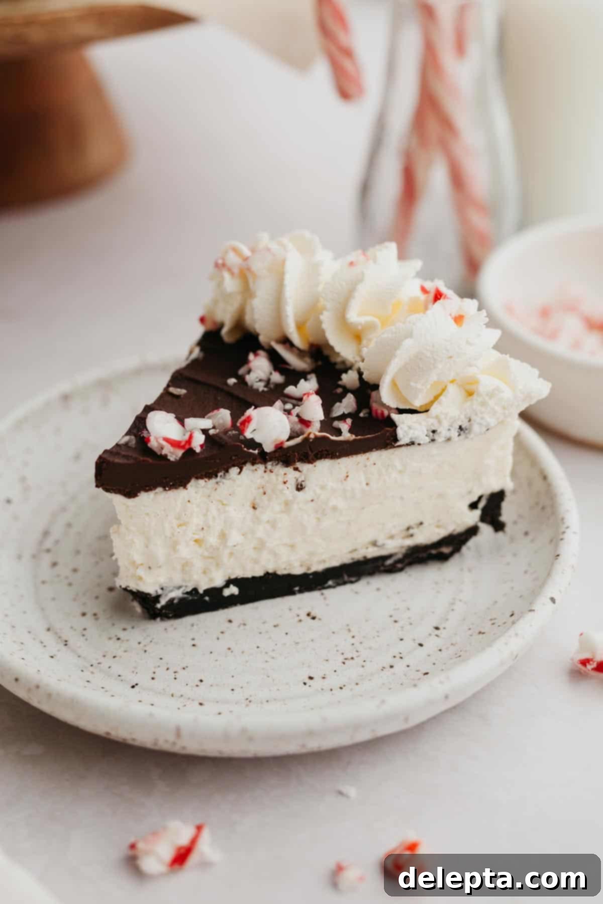 Candy Cane Crunch Cheesecake 2 A slice of peppermint bark cheesecake on a small plate, showing the distinct layers of crust, filling, and topping.