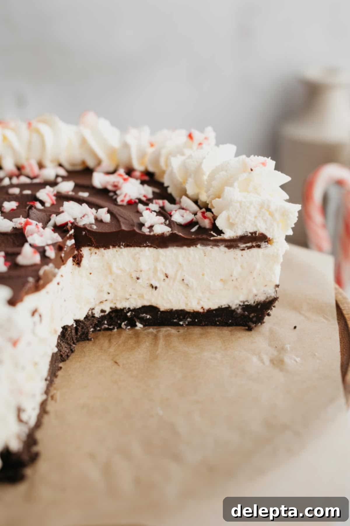 Candy Cane Crunch Cheesecake 8 A close up of a peppermint bark cheesecake which has been cut, showing the inside layers of crust, white filling, and chocolate topping.