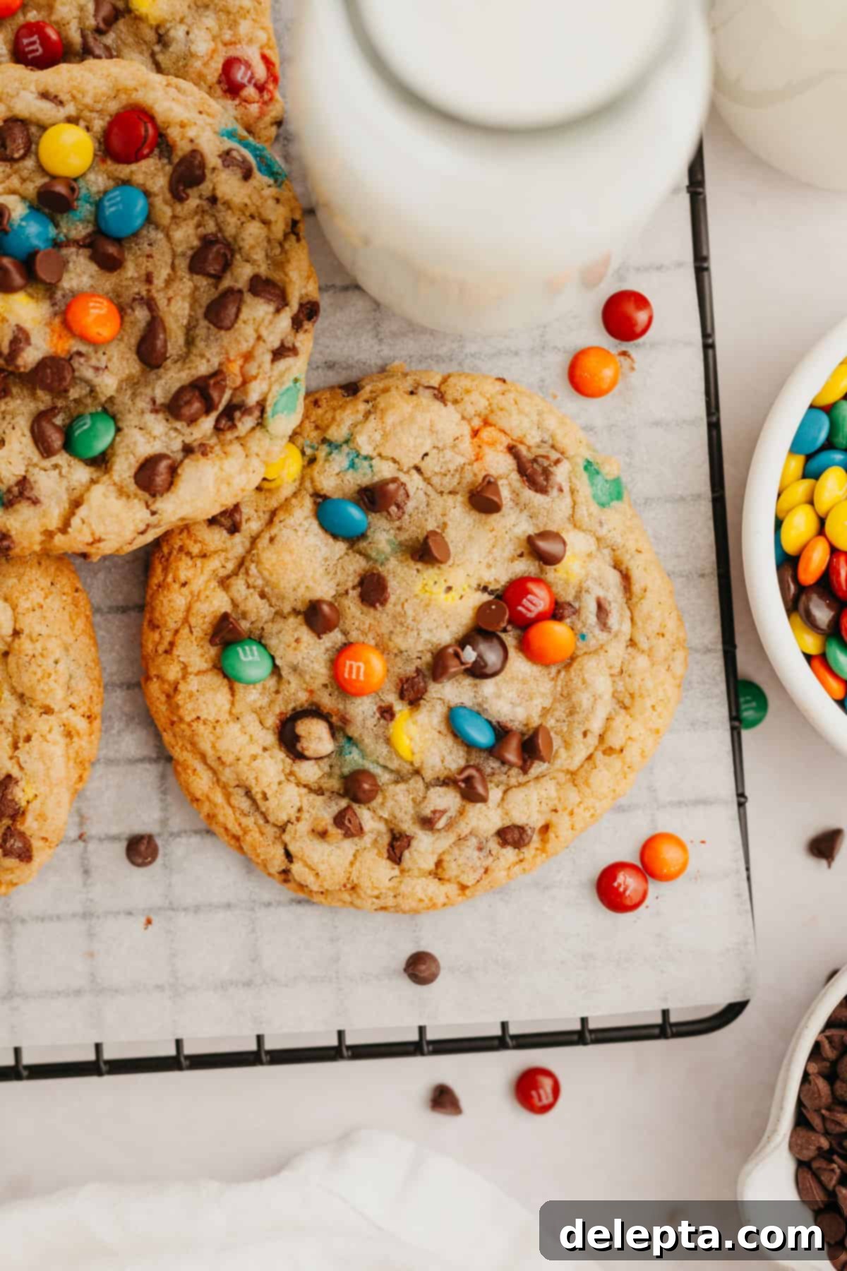 One-Bowl Rainbow Chip Cookie Delight 2 M&M chocolate chip cookies on parchment paper. A perfect batch of soft and chewy M&M cookies fresh from the oven, scattered with colorful candies and chocolate chips.