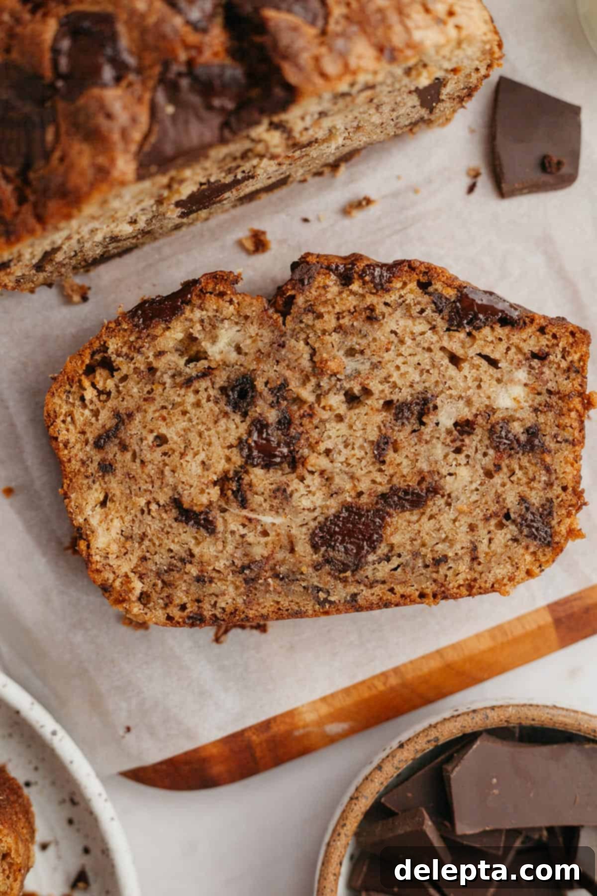 Seriously Moist Chocolate Chunk Banana Bread 2 A perfectly sliced piece of chocolate chunk banana bread resting on parchment paper, revealing a soft, moist interior and abundant chocolate chunks.