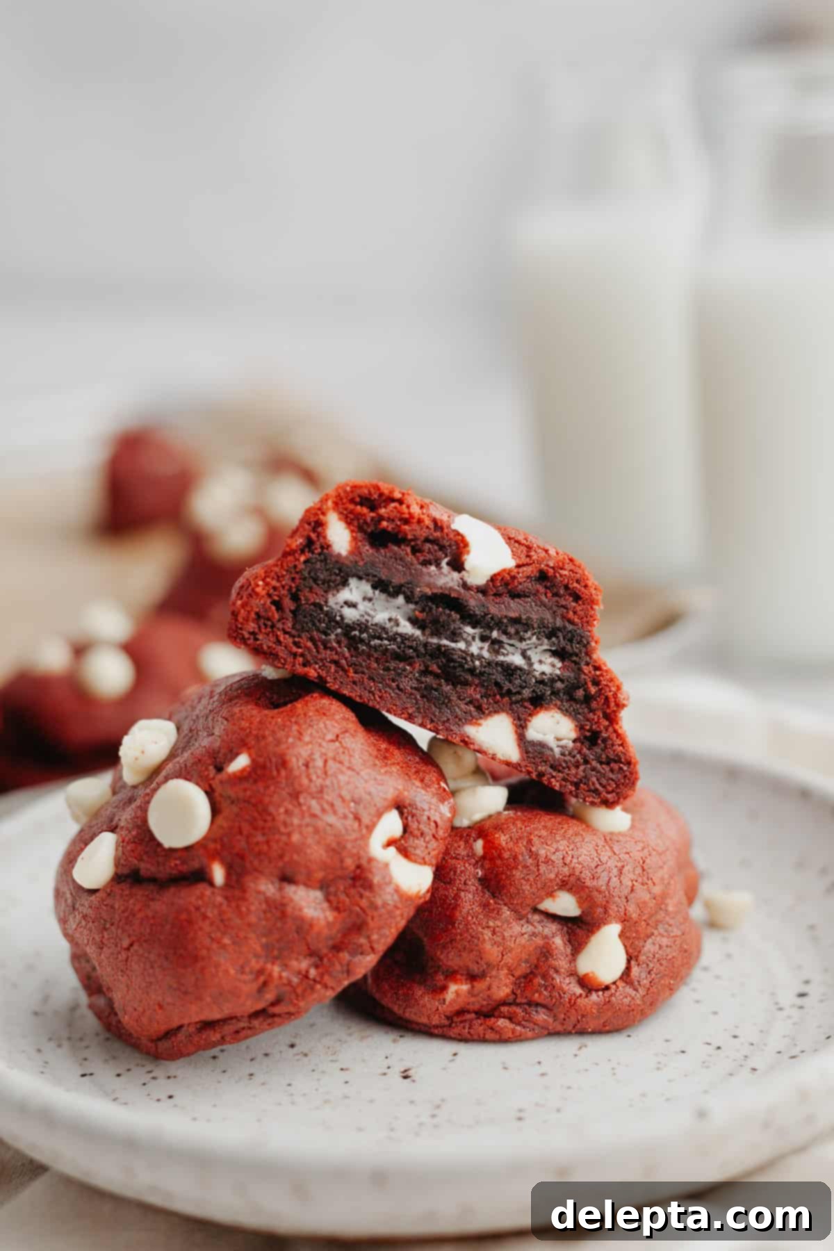 Homemade Red Velvet Oreo Cookies 2 Three red velvet cookies on a plate, one is cut in half showing it is stuffed with an Oreo.