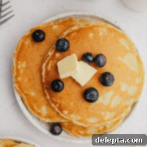 Decadent Sweet Cream Pancakes 8 A small plate showcasing three perfectly cooked sweet cream pancakes, garnished with fresh blueberries.