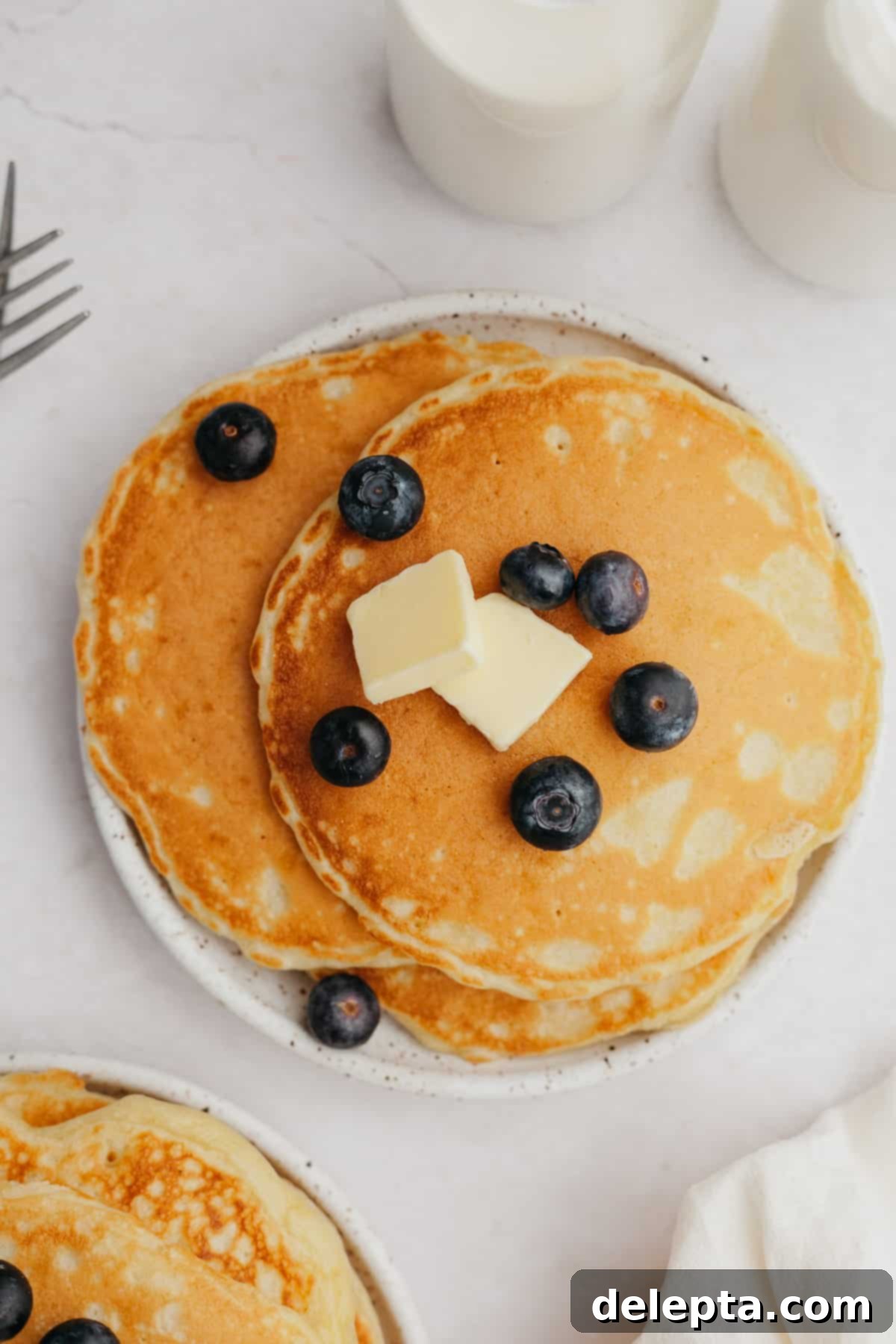 Decadent Sweet Cream Pancakes 7 A small plate showcasing three perfectly cooked, golden-brown sweet cream pancakes, beautifully garnished with a scattering of fresh blueberries.