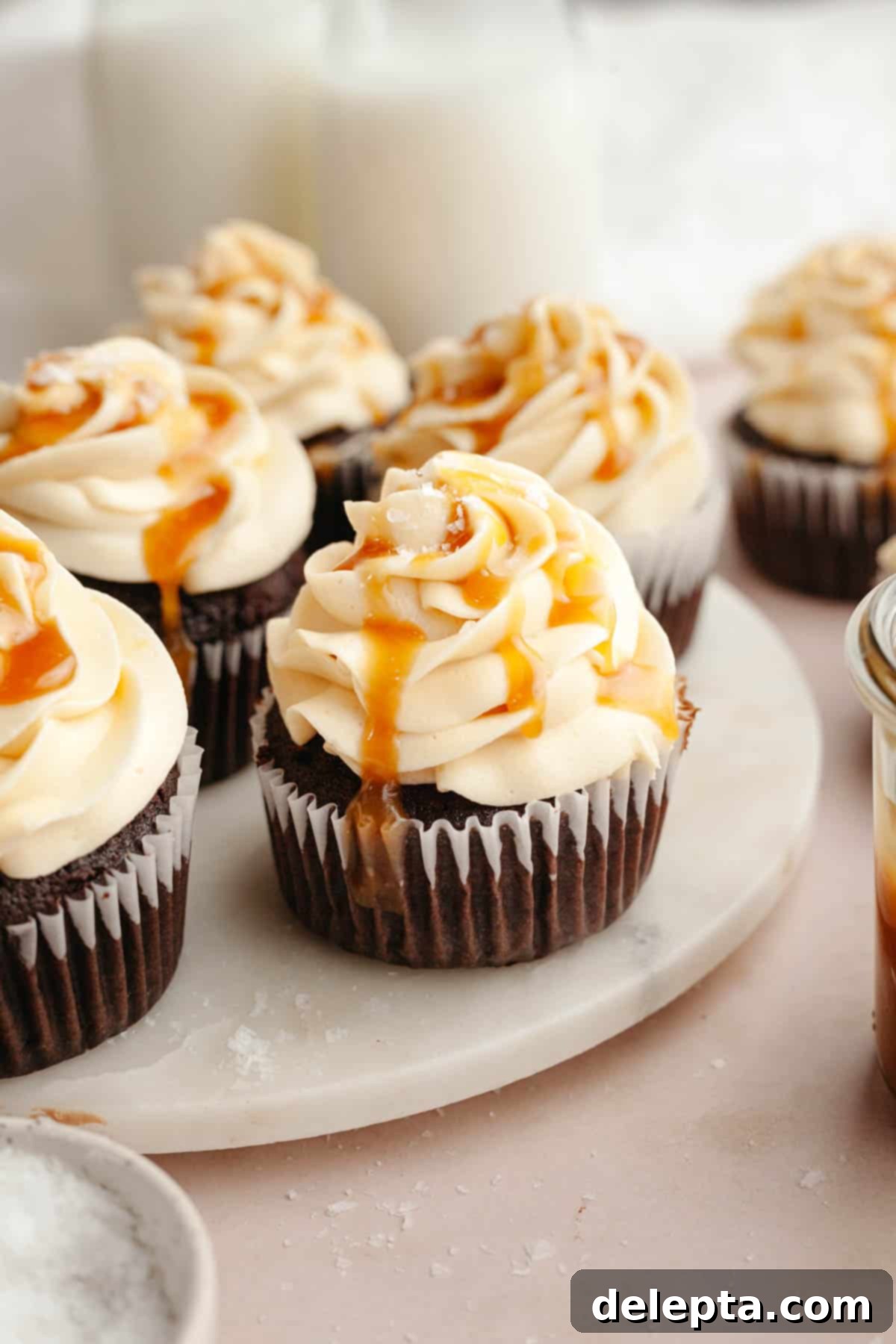Decadent Chocolate Salted Caramel Cupcakes 2 Decadent chocolate cupcakes topped with swirls of salted caramel buttercream, elegantly presented on a white marble surface.