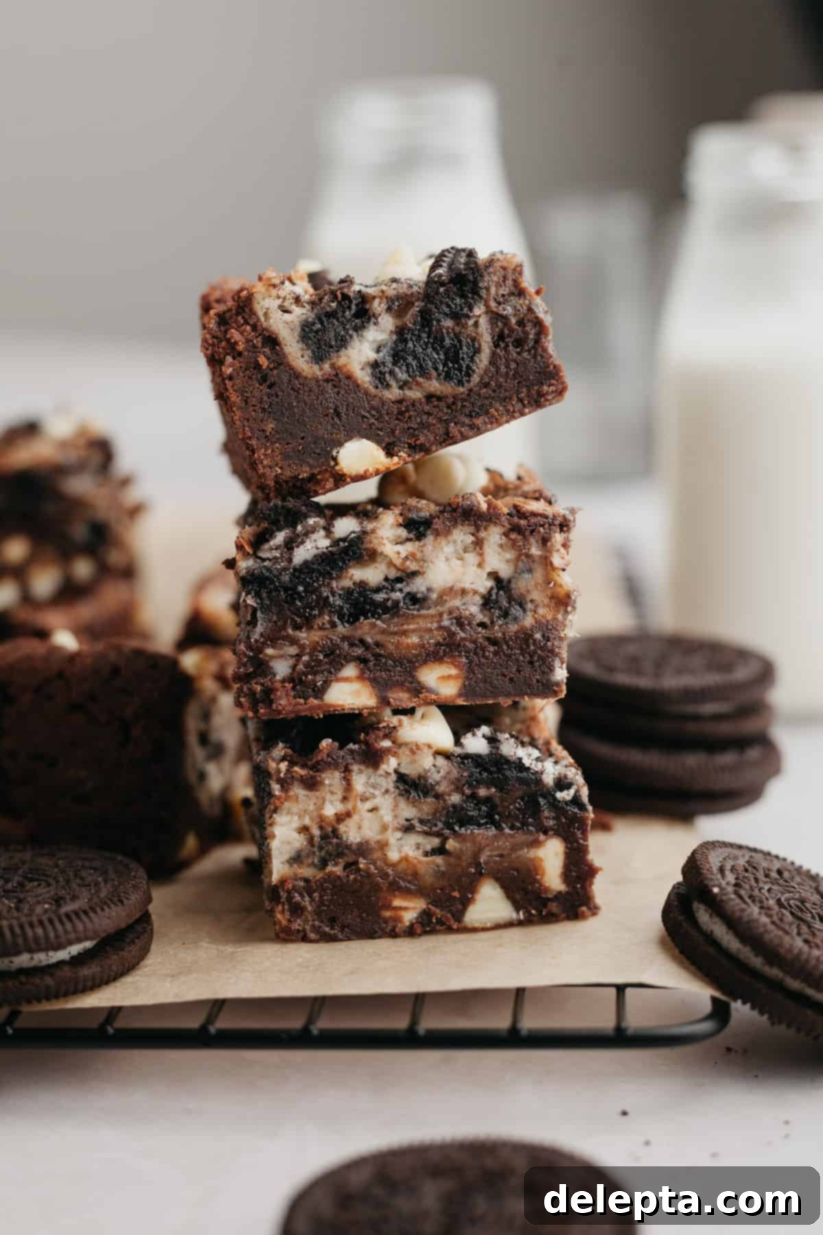 Oreo Cheesecake Swirl Brownies 2 A stack of three Oreo cheesecake brownies on parchment paper, showing the fudgy base and swirled cheesecake topping.