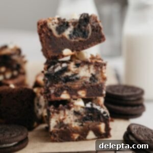 Oreo Cheesecake Swirl Brownies 9 A stack of three Oreo cheesecake brownies on parchment paper, highlighting the fudgy base and swirled cheesecake topping.