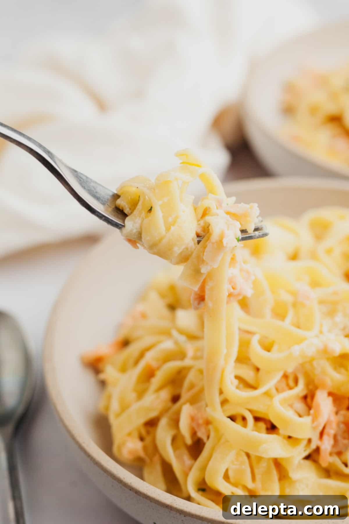 Creamy Salmon Pasta with Crème Fraîche 6 A close up of a fork pulling up pasta, showcasing the creamy sauce and salmon pieces.