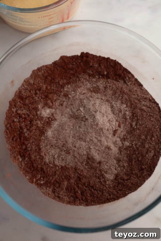 A large glass bowl containing a perfectly combined mix of cocoa powder and flour, along with other dry ingredients for the chocolate peppermint cake.