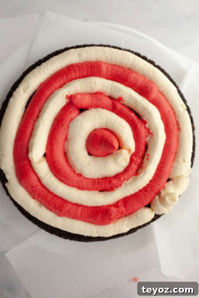 A chocolate cake layer meticulously frosted with alternating red and white concentric circles, expertly creating a bullseye pattern for the signature candy cane filling, on a white cake stand.