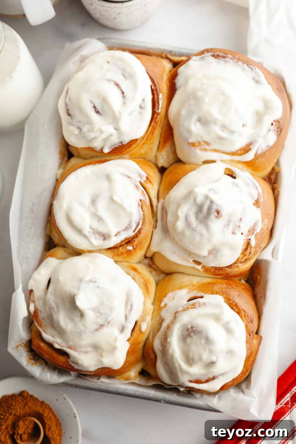 Six cinnamon buns covered in cream cheese icing in a small pan, showcasing their gooey texture.