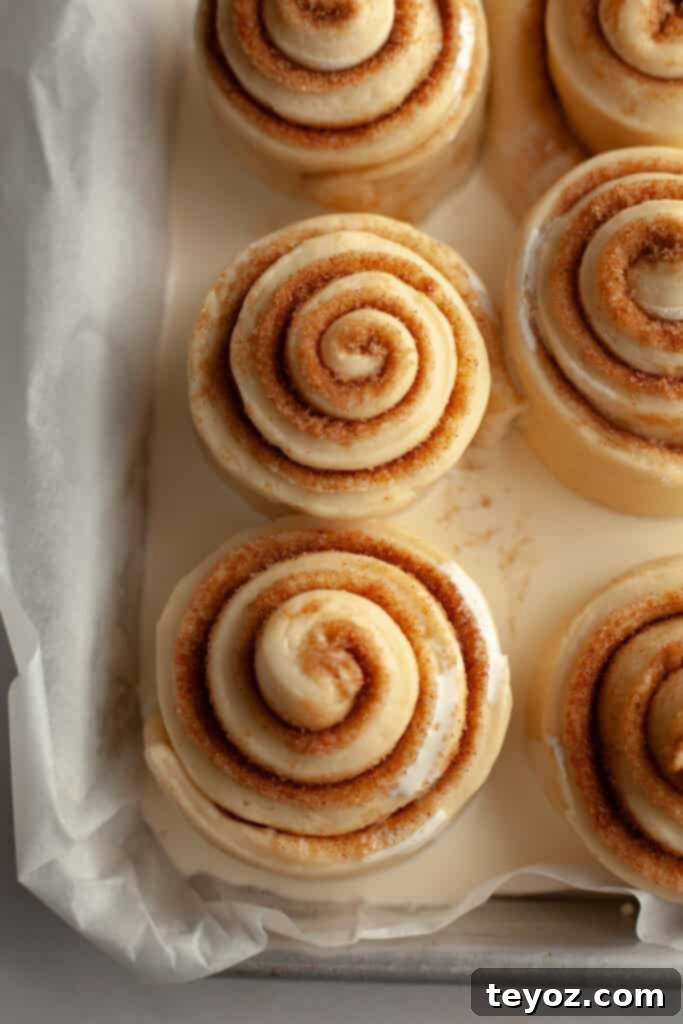 Unbaked cinnamon rolls in a small pan with heavy cream poured over them, ready for baking.