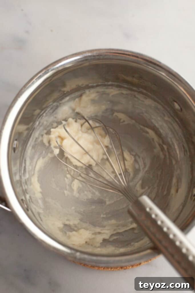 A small silver saucepan with a whisk and tangzhong batter in it, showing the initial stage of cooking the roux.