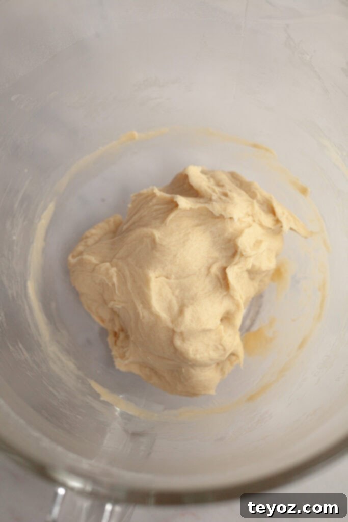 Cinnamon roll dough in a glass bowl after initial mixing, showing its developing texture.