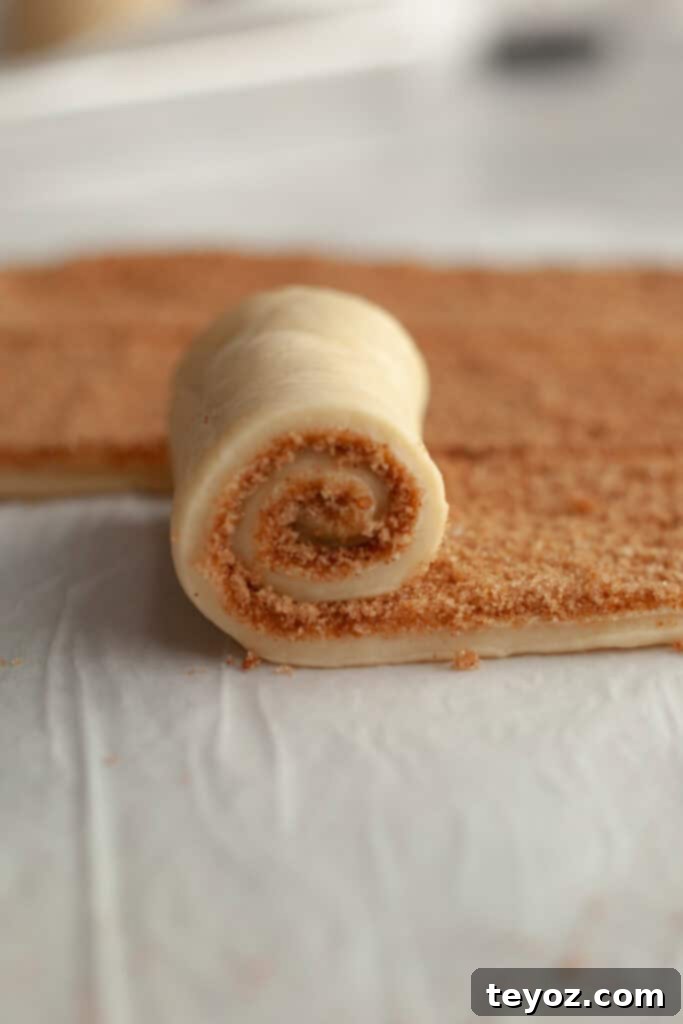 A cinnamon roll being rolled up, showing the tight spiral of dough and filling.