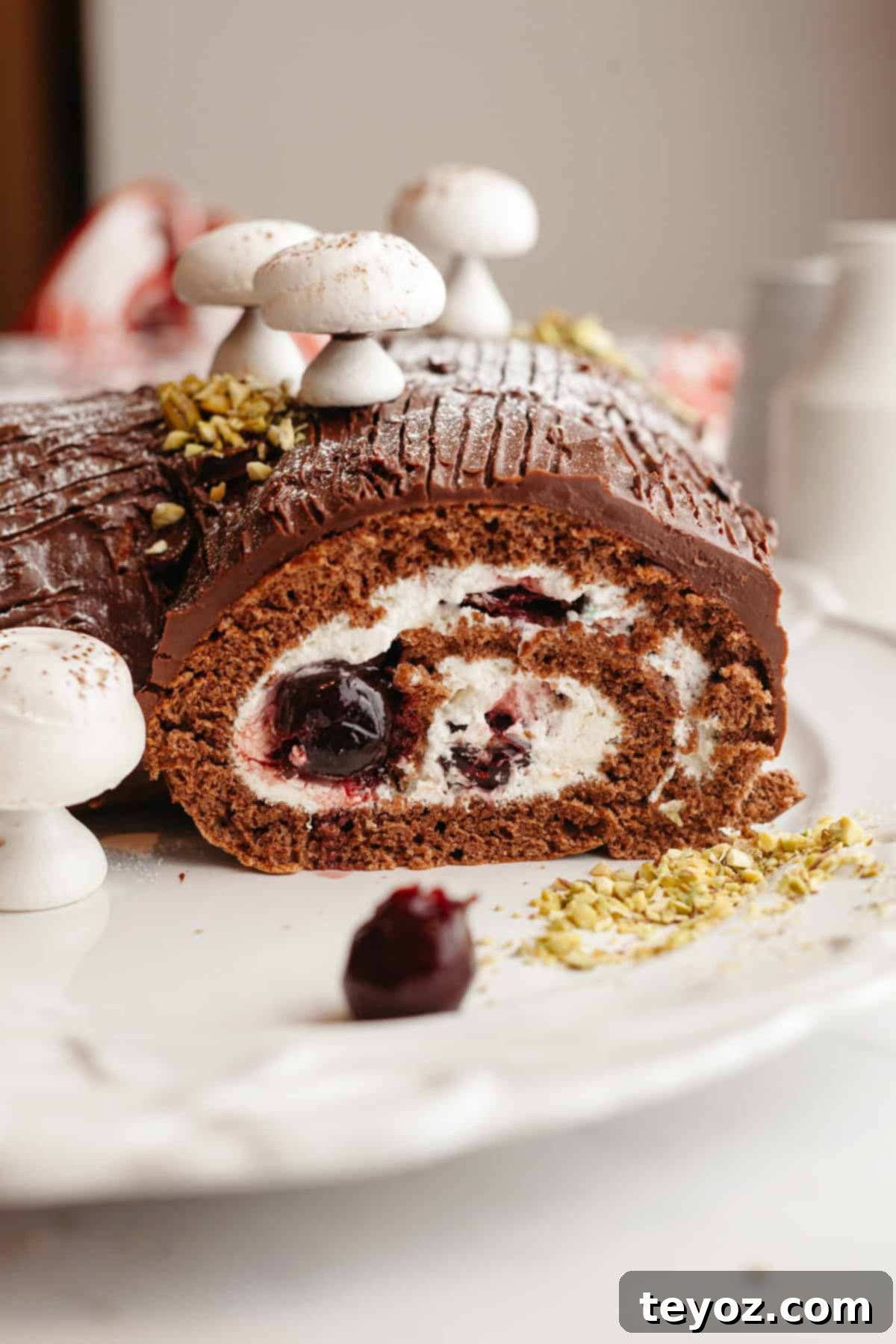 Aşağıdaki başlığı İngilizce'ye çevir ve özgünleştir: Black Forest Yule Log (Bûche de Nöel) Dark Chocolate Cherry Yule Log 2 A sliced black forest yule log with meringue mushrooms on a white plate, showcasing the layers of chocolate cake, whipped cream, and cherries.