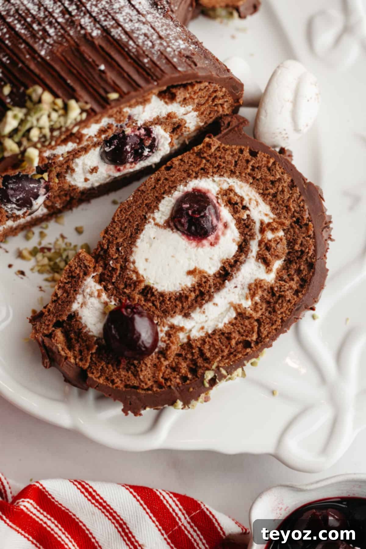 Aşağıdaki başlığı İngilizce'ye çevir ve özgünleştir: Black Forest Yule Log (Bûche de Nöel) Dark Chocolate Cherry Yule Log 14 A close up of a slice of black forest yule log on a white serving platter, revealing the delicious layers of chocolate cake, whipped cream, and cherries.