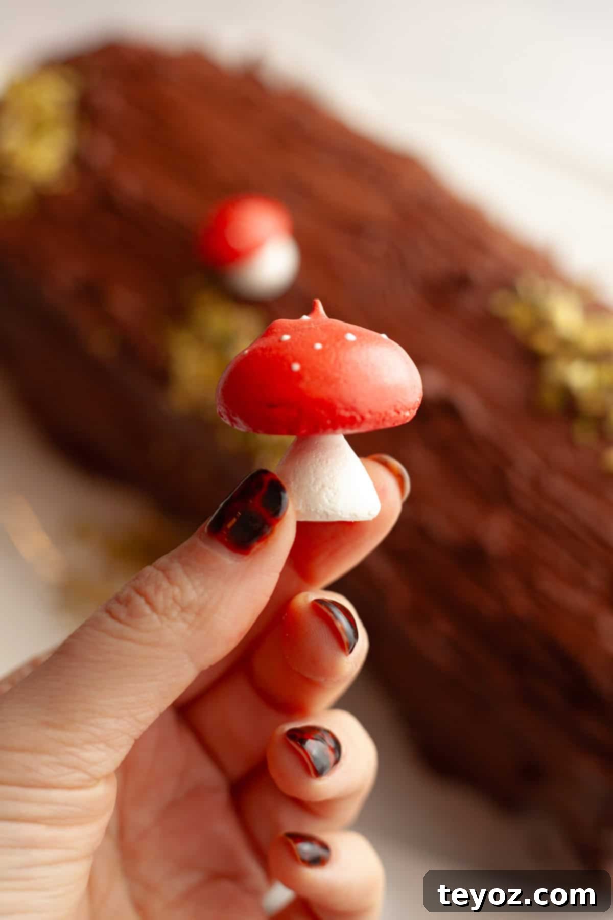 A hand holding a small meringue mushroom with a red cap and white stalk.