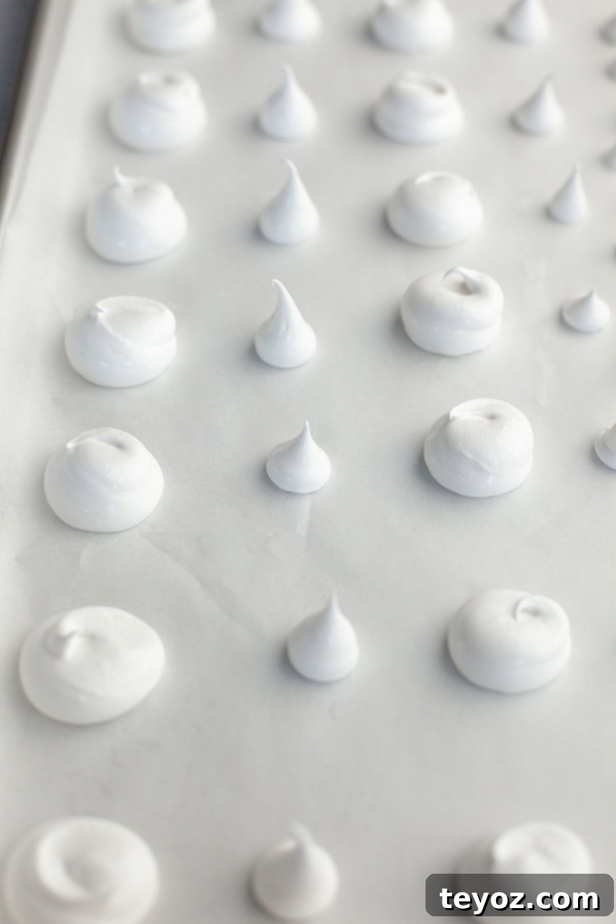 A parchment lined baking sheet with piped out meringue mushroom tops and stalks.