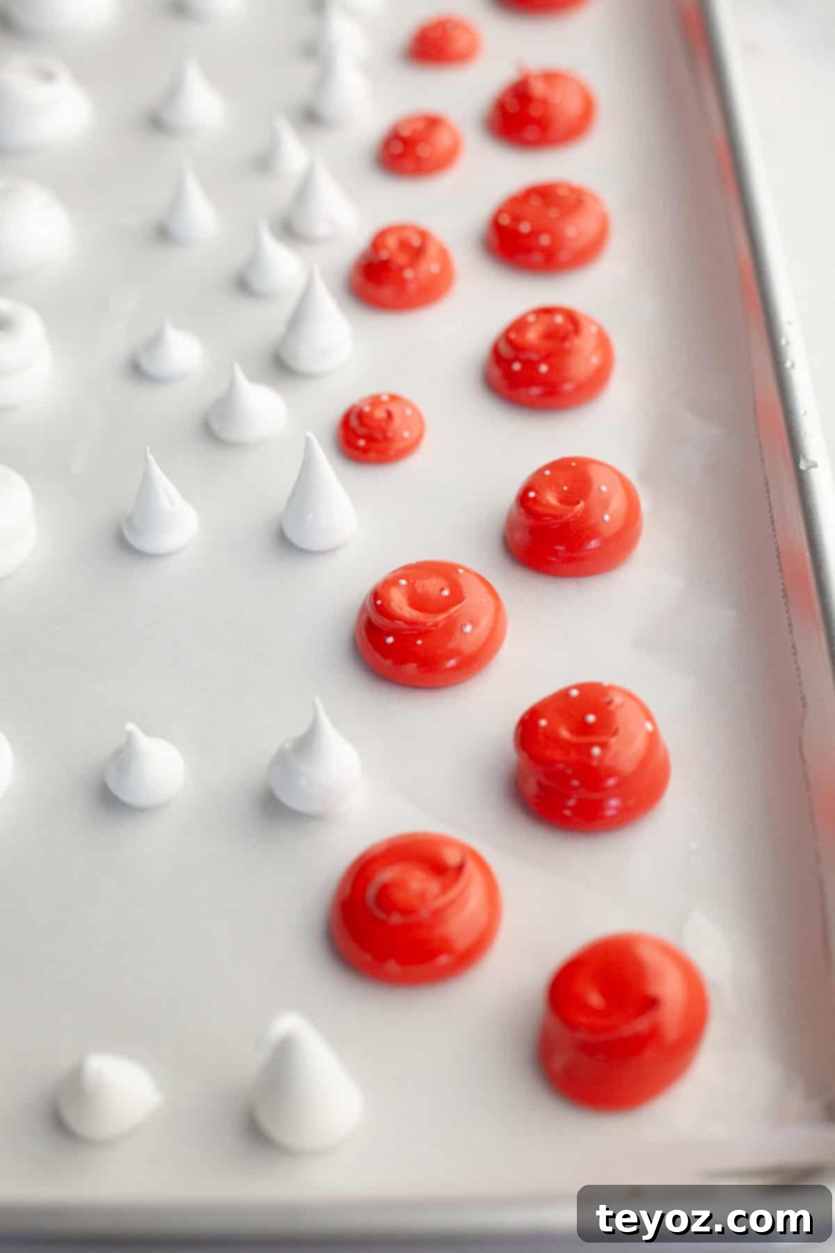A parchment lined baking sheet with piped out red meringue mushroom tops and white stalks.