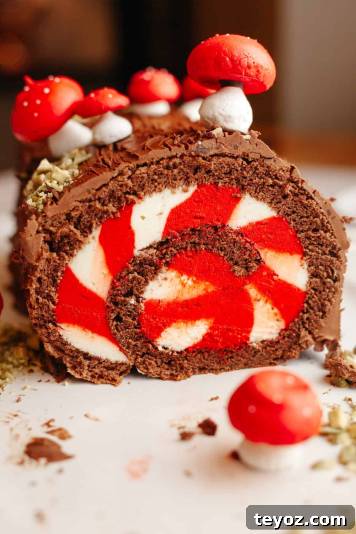A chocolate yule log with white and red striped filling, decorated with meringue mushrooms on a white platter.