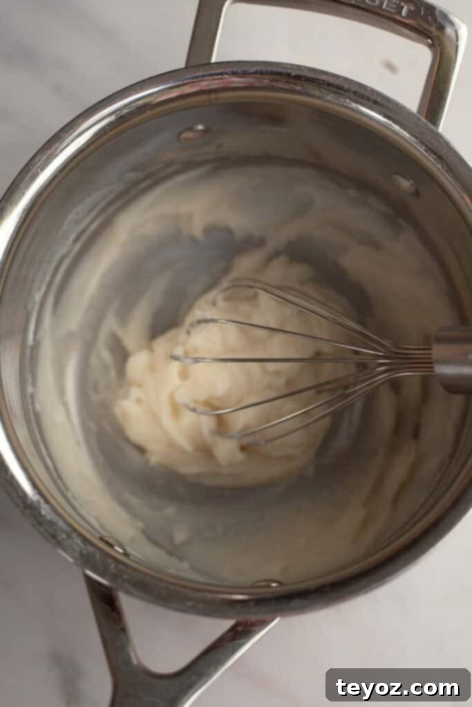 A silver saucepan containing dough and a whisk, illustrating the initial steps of making the Tangzhong.