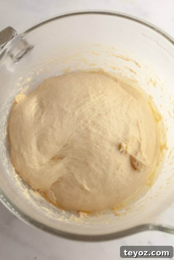 A close-up of cinnamon roll dough in a glass bowl, highlighting its smooth and elastic consistency after rising.