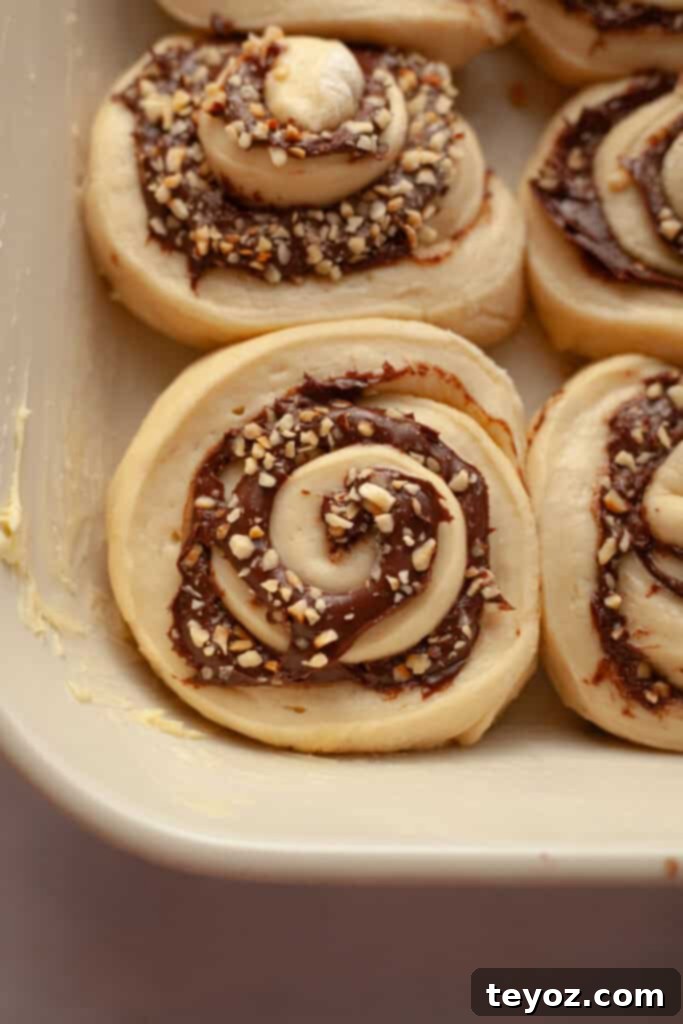 A close-up view of unbaked Nutella cinnamon rolls arranged in a white baking dish, ready to be proofed and baked to golden perfection.