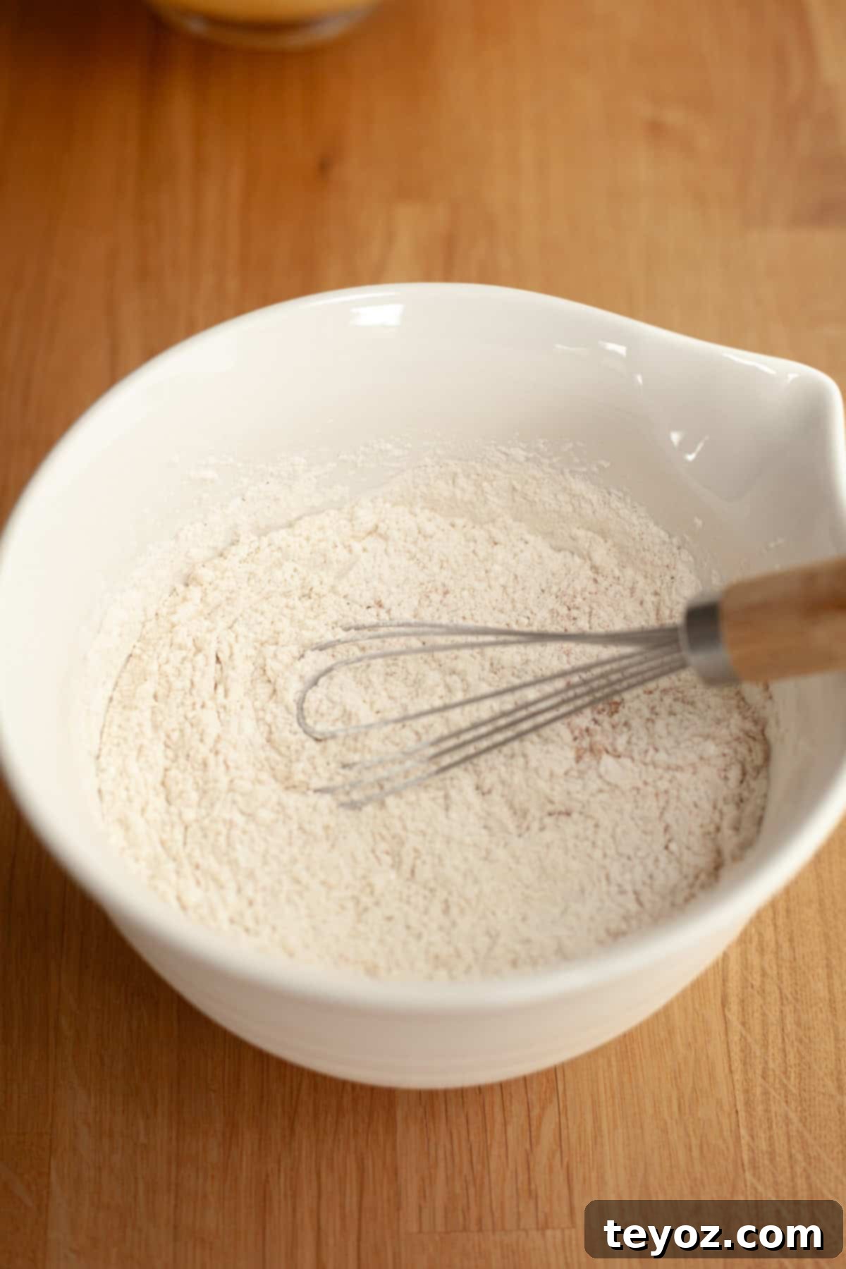 A clean white bowl holds a whisk and a generous pile of flour, a visual representation of the dry ingredients coming together in preparation for cinnamon shortbread cookies.